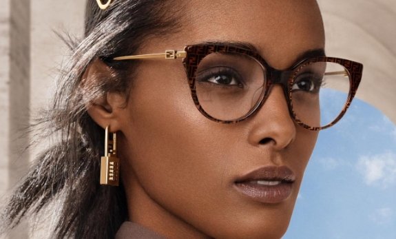Mulher negra com brincos dourados usando óculos de grau estilo gatinho marca fendi com hastes douradas e armação marrom