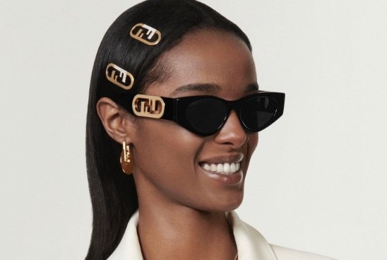Mulher negra em fundo branco usando grampos de cabelo e óculos de sol da marca fendi com detalhes nas hastes