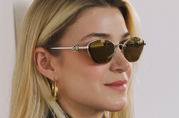Mulher com cabelos loiros sorrindo usando óculos de sol da marca Loewe